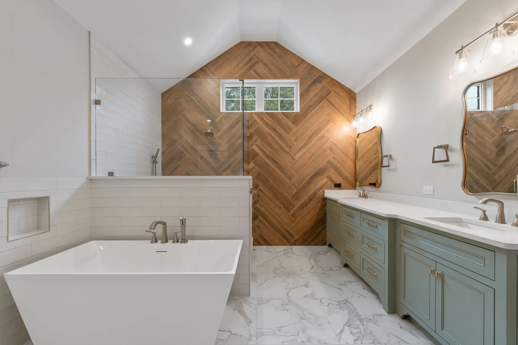 Luxury master bathroom interior photo in Pfafftown NC featuring freestanding soaking tub, herringbone wood tile accent wall, sage green double vanity, and marble floors